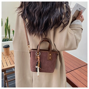 Détail du sac seau en daim marron vintage avec matelassage et pompon en bois