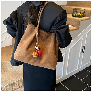 Close-up of brown suede tote bag featuring colorful plush pom-pom charms and brand logo