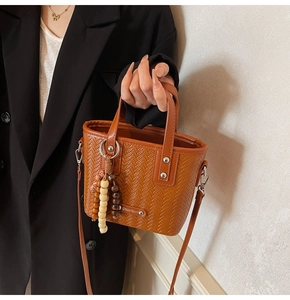 Détail d'un sac à main marron tressé avec breloque en bois et bandoulière amovible