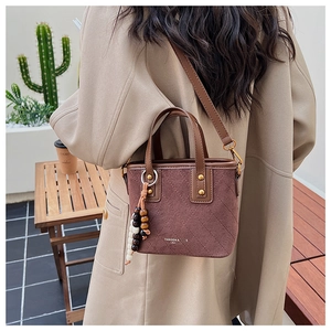 Détail du sac seau bordeaux en daim avec motifs matelassés et pompon en perles de bois