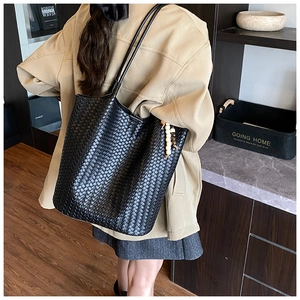 Detail of a black woven leather tote bag with elegant beaded charm accessory