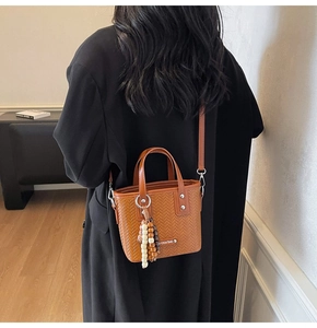 Détail du sac seau tressé marron avec breloque en perles de bois et bandoulière longue