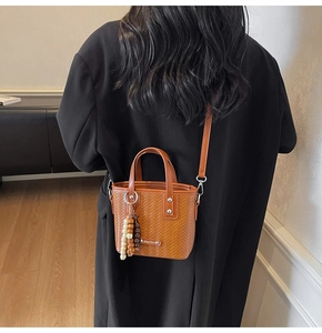Détail du sac tressé marron avec pendentif en perles et plaque logo en métal poli