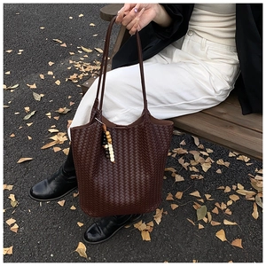 Detail of a brown woven tote bag with beaded charm on an outdoor wooden bench
