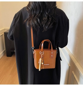 Détail d'un sac seau tressé marron avec pendentif en perles de bois et fine bandoulière chic