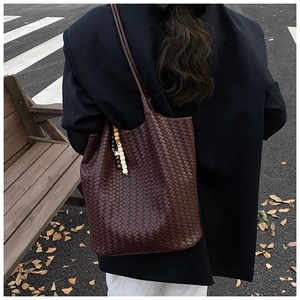 Detail of dark brown woven leather tote bag with colorful bead charm on a shoulder strap