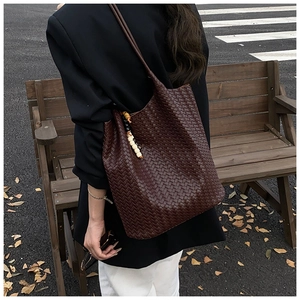 Detail of a dark brown woven tote bag featuring a vintage beaded wooden charm accessory