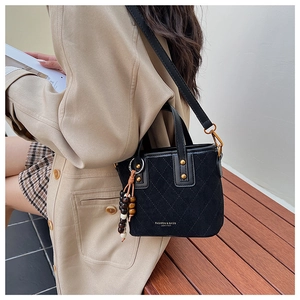 Détail du sac seau noir en daim matelassé avec perles en bois et logo de mode