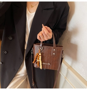 Détail d'un sac à main marron tressé avec breloque en perles et bandoulière réglable