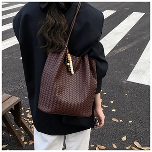 Street style shot of a brown woven leather tote bag with colorful bead charm on shoulder
