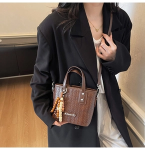 Détail d'un sac seau tressé marron foncé avec perles en bois et emblème métallique