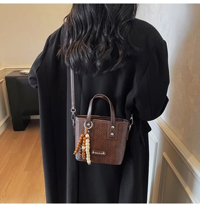 Détail du sac cabas tressé marron foncé avec pompon en perles sur un manteau noir
