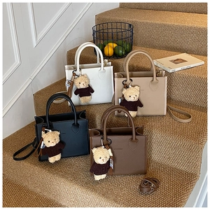 Detail view of four-color textured tote bags with bear charms and shoulder straps