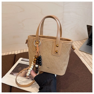 Détail du sac seau en daim marron avec surpiqûres matelassées et pendentif en perles
