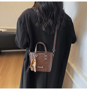 Détail du sac seau tissé avec logo métallique chic et accessoire pompon en perles de bois
