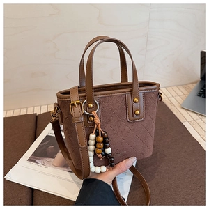 Gros plan du sac seau en daim marron avec motifs matelassés et détails de glands perlés