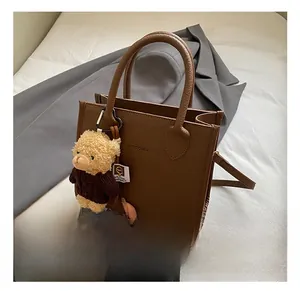 Detailed view of a brown pebbled leather tote bag featuring a cute teddy bear charm