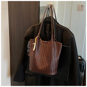 Macro detail of dark brown hand-woven leather tote with colorful bead charm on a coat