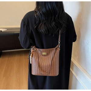 Detail einer braunen geflochtenen Eimertasche mit Holzperlen und langem Schultergurt