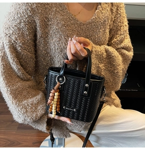 Détail de la texture tressée du sac seau noir avec breloque perle et plaque logo