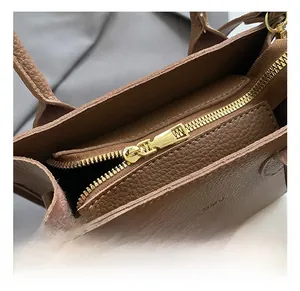 Detail of brown litchi leather handbag showing golden zipper and metal hardware quality