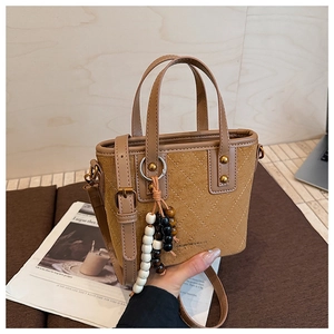 Détail du sac seau en daim vintage avec motifs matelassés et porte-clés décoratif perlé