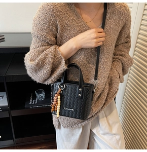 Détail du sac noir tressé avec breloque en perles de bois et bandoulière longue
