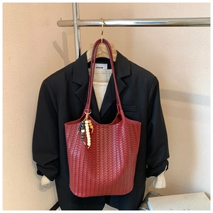 Deep red woven tote bag with wooden bead tassel hanging on a black suit jacket