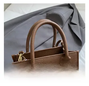 Detail of brown litchi pattern leather tote bag with sturdy double handles and gold hardware