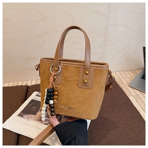 Détail du sac seau en daim marron avec texture matelassée et breloque en perles de bois