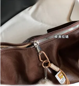Detail of vintage brown faux leather tote bag with smooth metal zipper and plush pompom charm