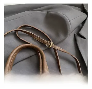 Detail of adjustable shoulder strap with gold buckle on brown lychee leather bucket bag