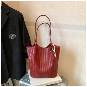 Detail view of red woven leather bucket bag with artistic tassel and slender handles
