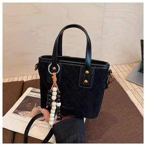 Détail du sac seau en daim noir avec motifs matelassés et breloque en perles de bois