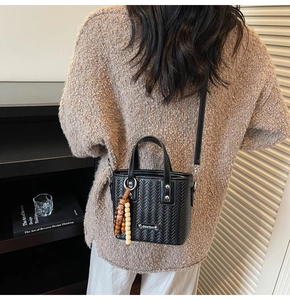 Détail d'un sac bandoulière noir à texture tressée avec pendentif et boucles en métal