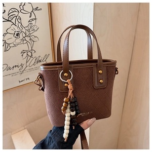 Détail du sac seau en daim marron avec surpiqûres en losanges et pendentif en perles