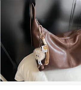 Detail of a brown leather hobo bag with zipper and a quirky plush monster charm
