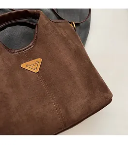Dettaglio borsa a secchiello in camoscio marrone scuro con logo triangolare dorato e cuoio