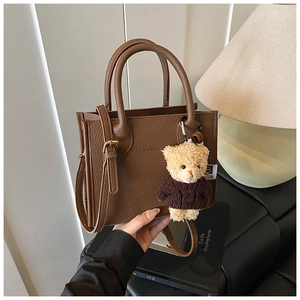 Detail of dark brown lychee texture leather bucket bag with a cute teddy bear pendant