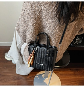 Détail du sac seau noir tissé avec plaque logo argentée et pendentif en perles de bois