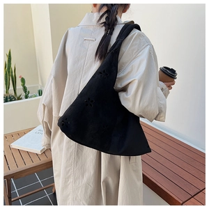 Close-up of black hollow-out hobo bag with wide shoulder strap on a model outdoors