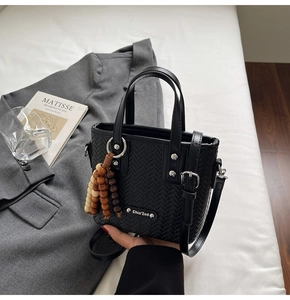 Détail du sac cabas tissé noir avec pompon en perles de bois sur literie blanche