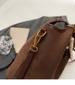 Dettaglio dei ganci dorati vintage e perline di legno su una borsa a secchiello in camoscio
