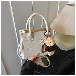 Detailed view of white lychee leather handbag with a bear charm and brand logo