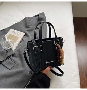 Détail du sac noir à texture tressée avec logo doré et pendentif en perles de bois