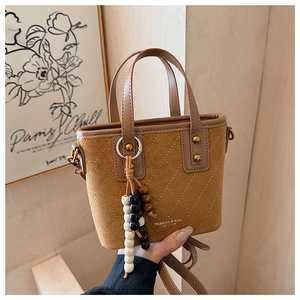 Détail du sac seau en suède avec coutures matelassées et accessoire pompon en perles