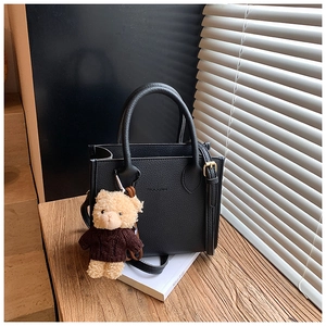 Detail of black lychee grain tote bag with embossed logo and cute bear charm decoration