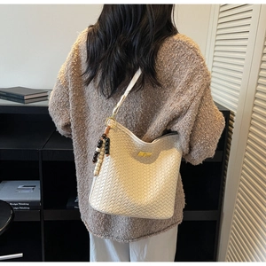 Detailaufnahme der beigen geflochtenen Eimertasche mit Metallschloss und Perlenanhänger