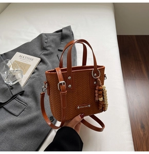 Détail d'un sac seau tressé marron avec logo argenté et pompon décoratif en perles