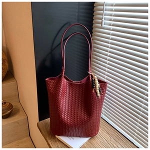 Close-up of woven wine red leather tote bag with wooden bead charm on a wooden table